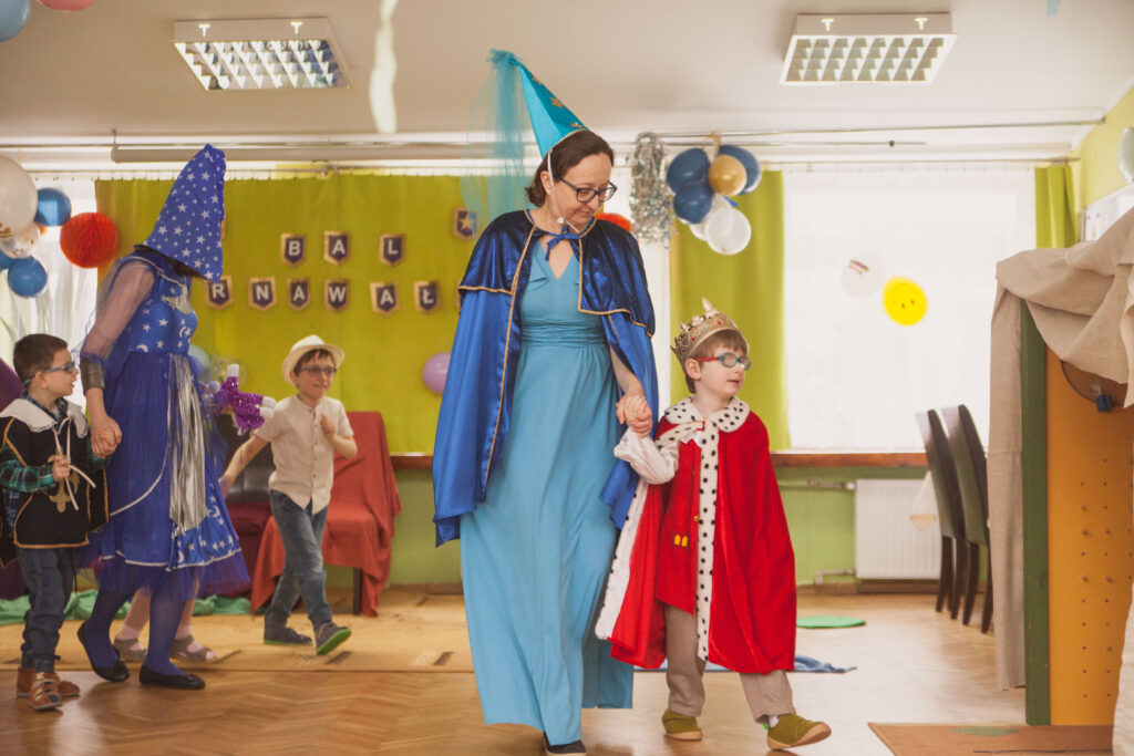Przebrana nauczycielka z przebranym za króla chłopcem w tle inni przebierańcy.