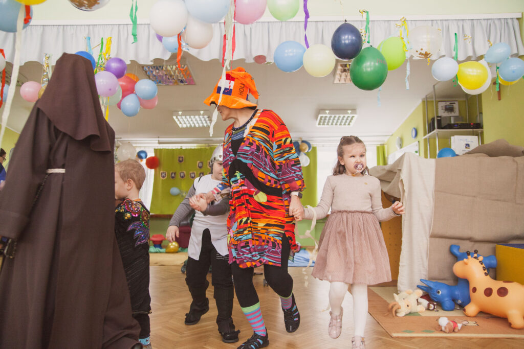 Przebrana nauczycielka trzyma za ręce dwoje przebranych dzieci. 