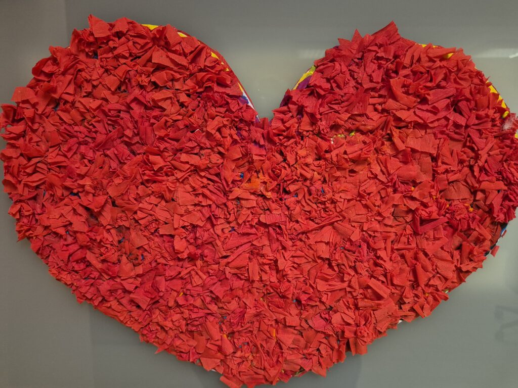 Skończone czerwone, duże serce oklejone plasteliną a w niej powbijane kawałeczki plasteliny