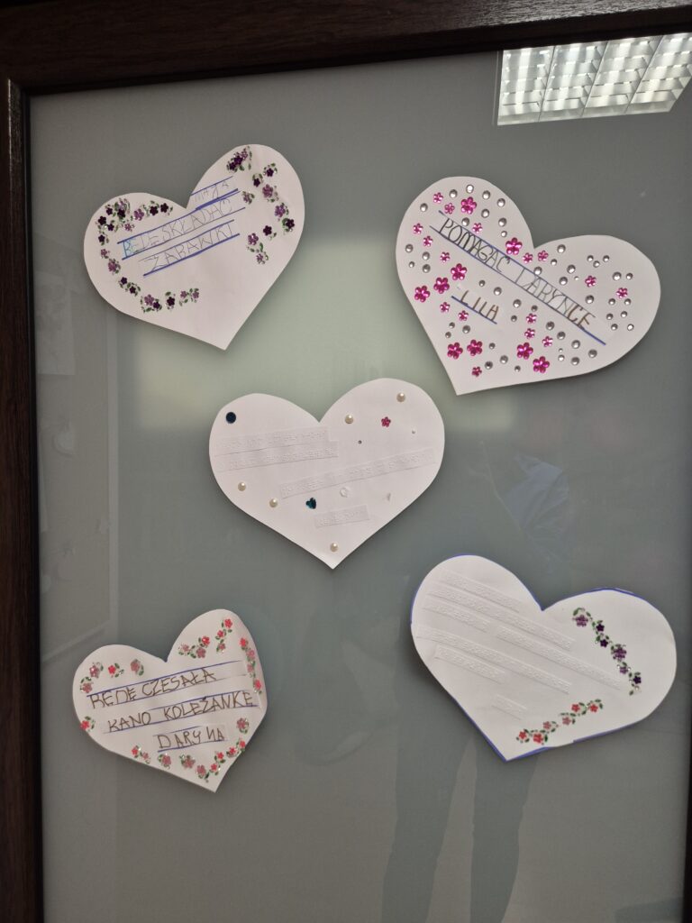 Białe serduszka powieszone w grupie I na drzwiach wejściowych. Na sercach ozdobionych koralikami, kwiatkami zapewnienia z dobrymi uczynkami