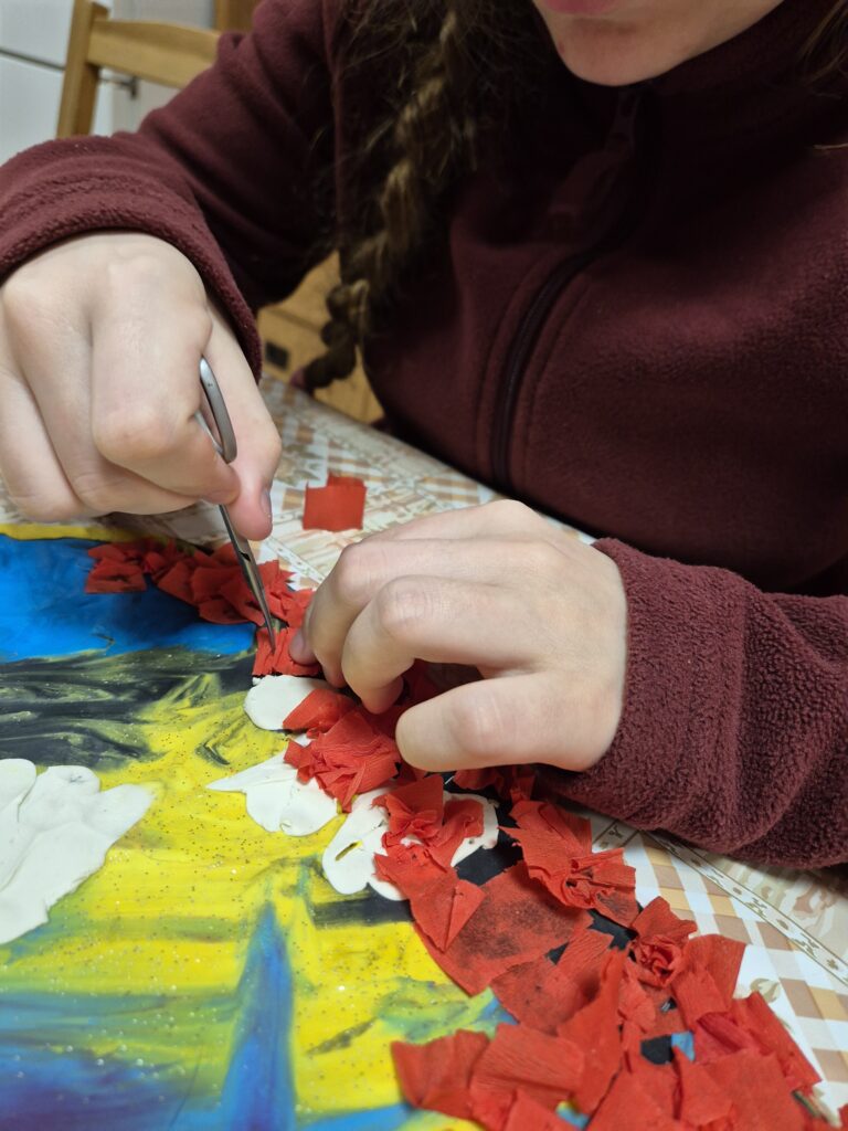 Julia kontynuuje dalsze wklejanie czerwonych bibułek w serce obklejone plasteliną