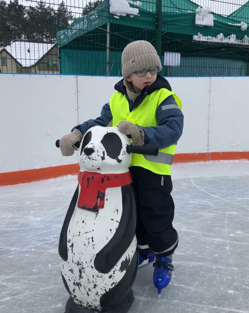 Chłopiec w łyżwach, stoi na lodowisku, przed nim pchacz- panda