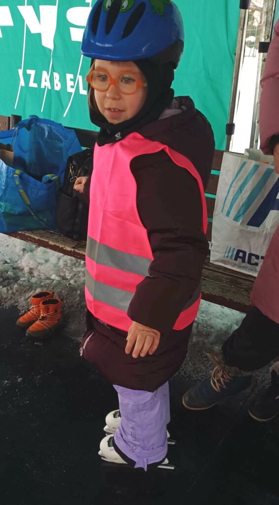 Dziewczynka w kasku i łyżwach, stoi obok ławki