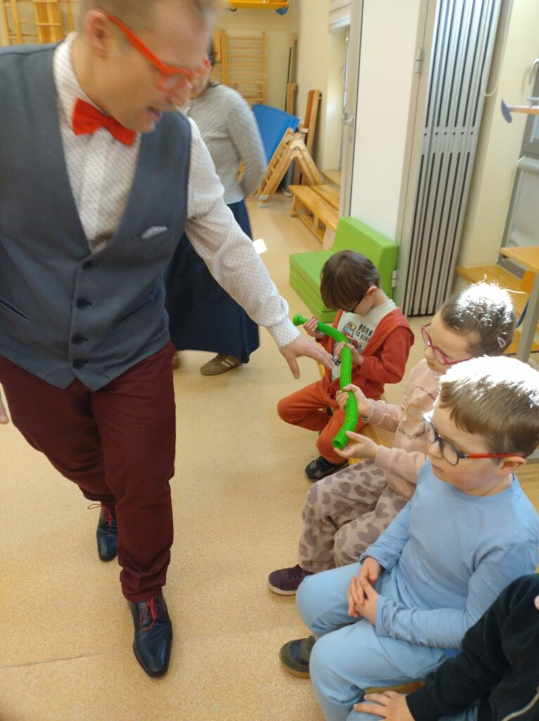 Prowadzący pokazuje dzieciom długą rozciągliwą rurkę