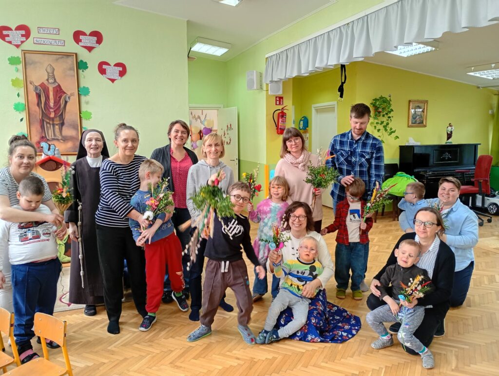 Zdjęcie grupowe rodziców, dzieci i nauczycieli  z palmami.