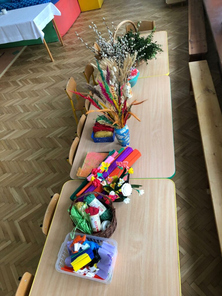 Stoły zastawione materiałami do robienia palm - bibuła, bazie, sznurki, zboża.