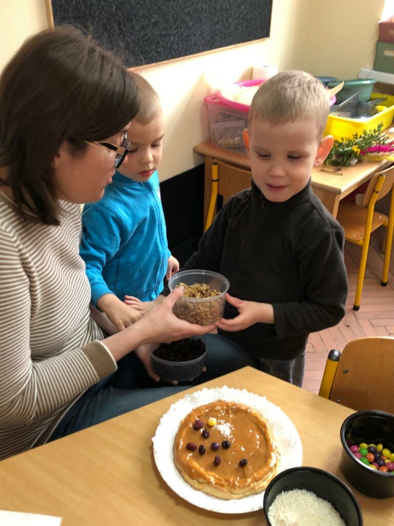 Dwóch chłopców z mama ozdabiają mazurek.