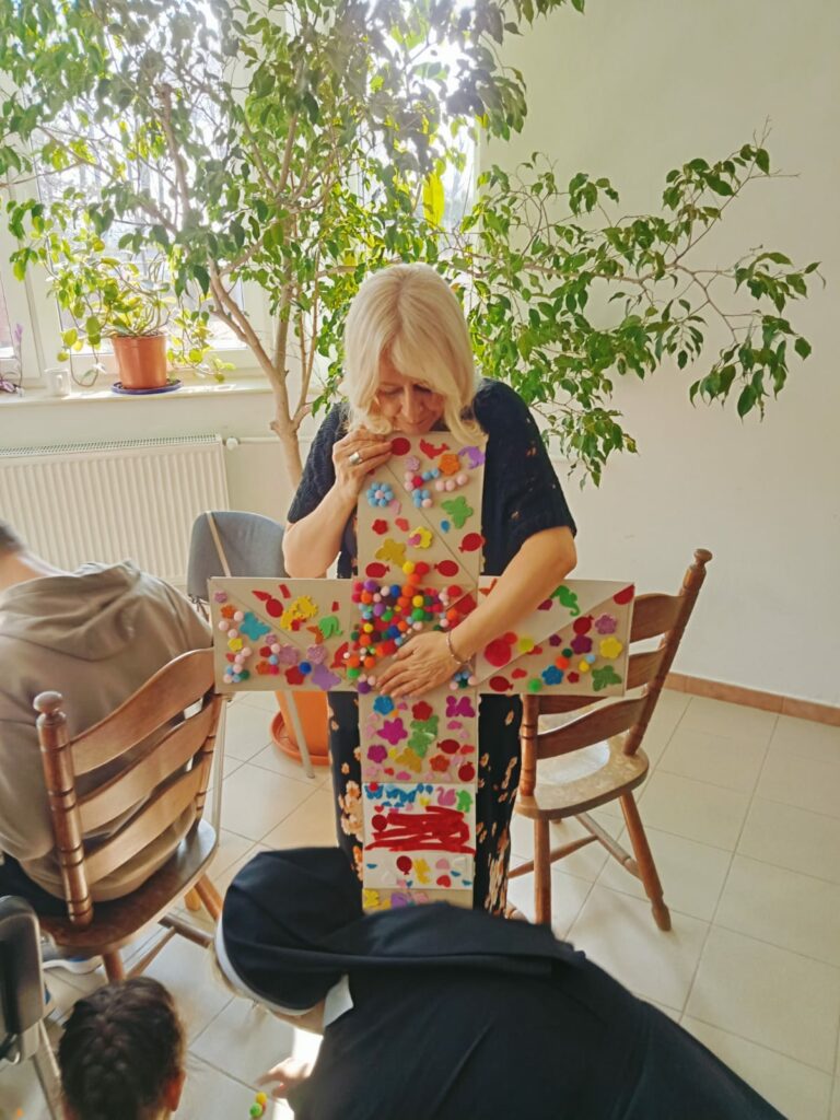 Przyklejanie kolorowych ozdób do tekturowego krzyża