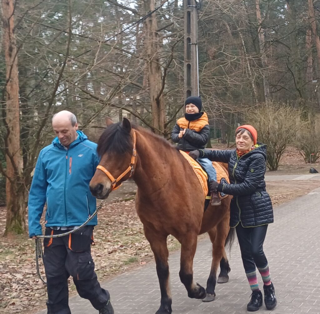 Chłopiec jedzie na koniu obok idą terapeuci 