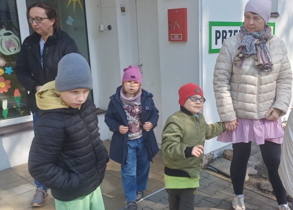 Dzieci z nauczycielkami przed budynkiem przedszkola.