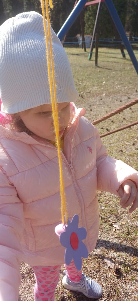 Dziewczynka a przed nią papierowy kwiatek na sznurku.