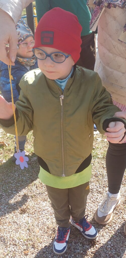 Chłopiec wyciąga rękę po papierowy kwiatek na sznurku.