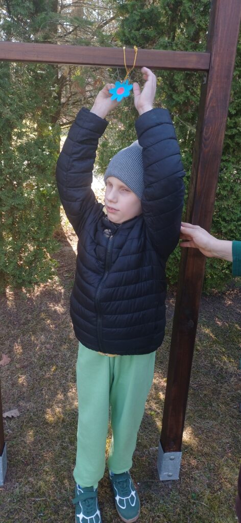 Chłopiec z wyciągniętymi rękami do góry trzyma papierowy kwiatek.