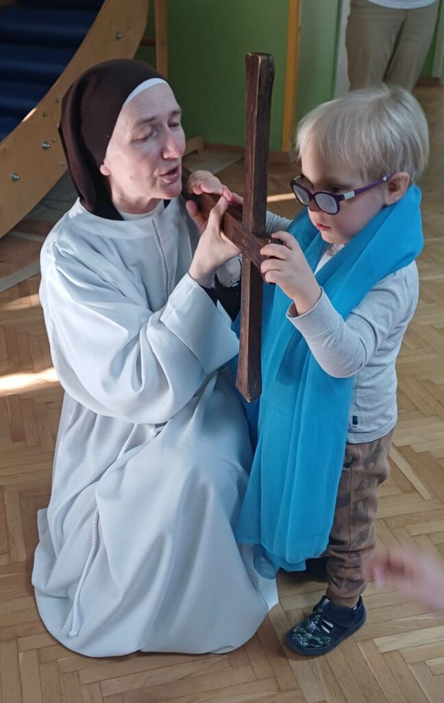 Chłopiec owinięty niebieskim szalem, obok siostra zakonna, razem trzymają krzyż