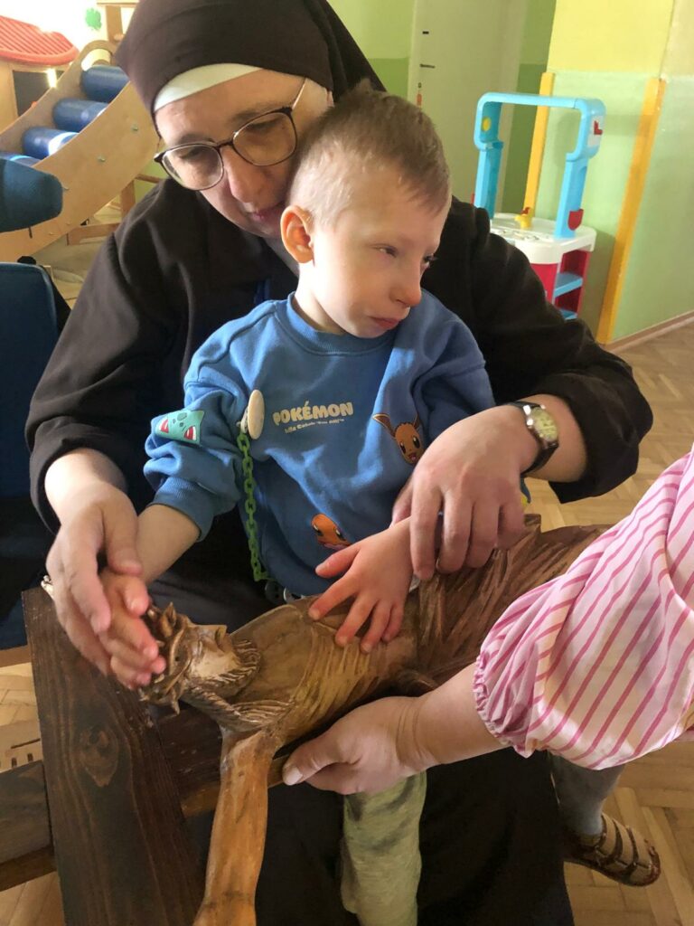 Chłopiec dotyka figury Pana Jezusa na krzyżu, za nim opiekunka 