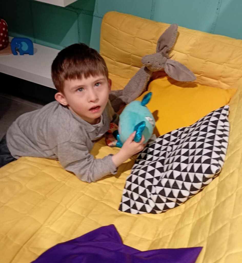 Chłopiec oparty o kanapę, trzyma w rękach maskotkę.