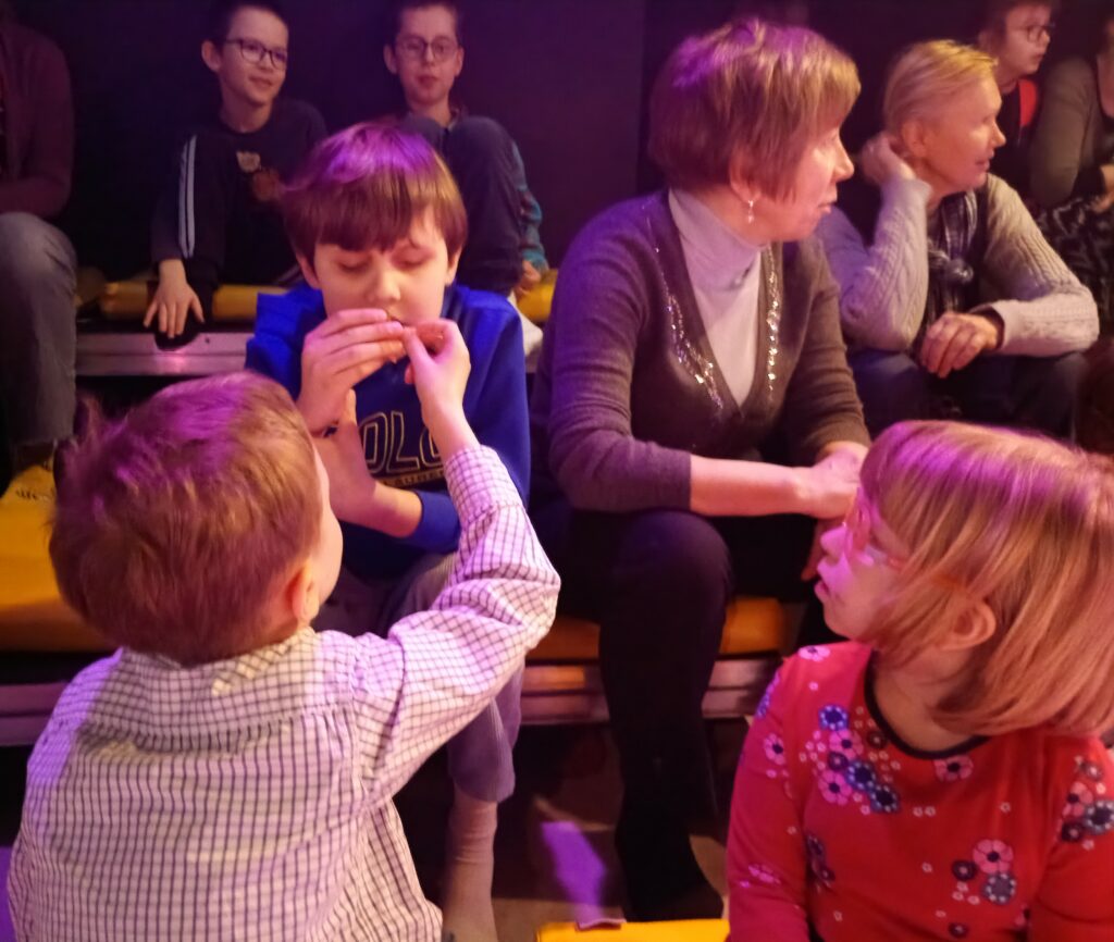 Chłopiec podaje koledze zapachową gwiazdkę, obok siedzi dziewczynka, za nią opiekunowie.