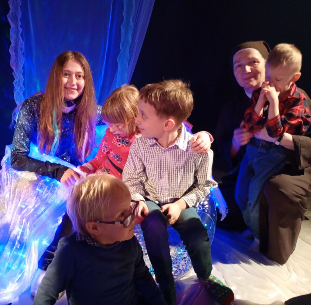 Dzieci, wychowawczyni i aktorka siedzą na elementach scenografii.