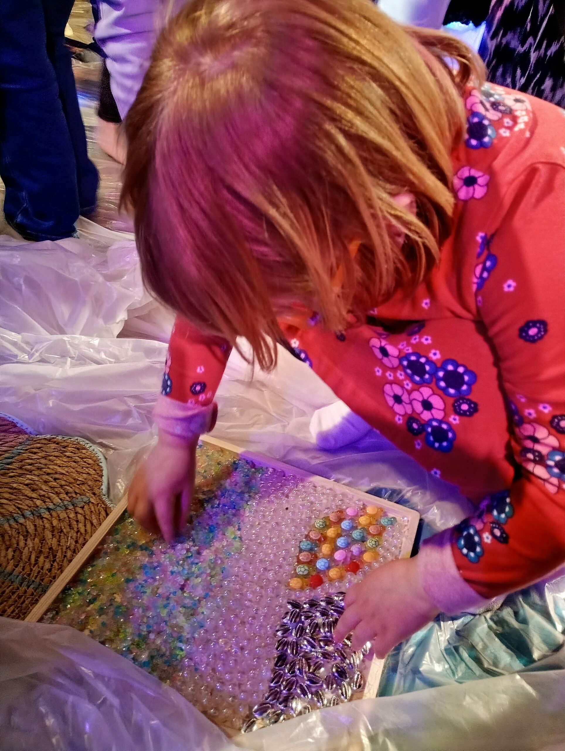 Kucająca dziewczynka dotyka sensorycznego panelu.