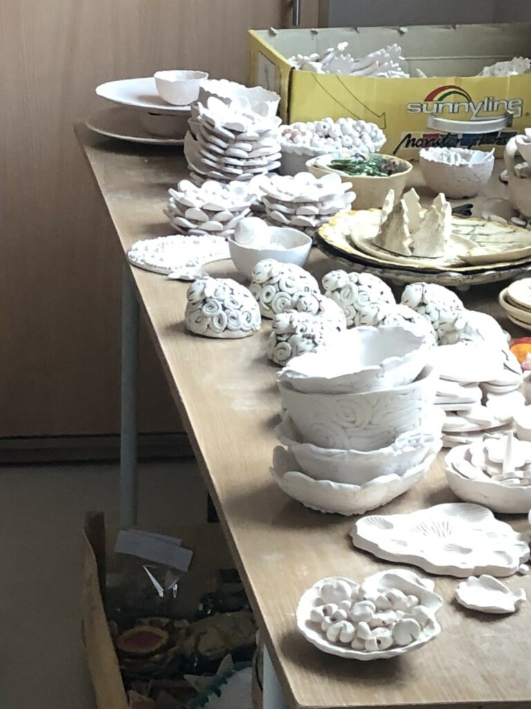 Stół zastawiony licznymi pracami z gliny. Prace mają biały kolor.