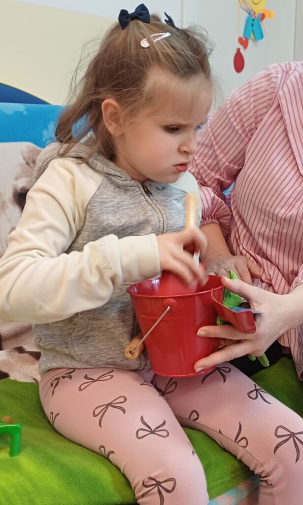 Dziewczynka ogląda metalowe, czerwone wiaderko i łopatkę.