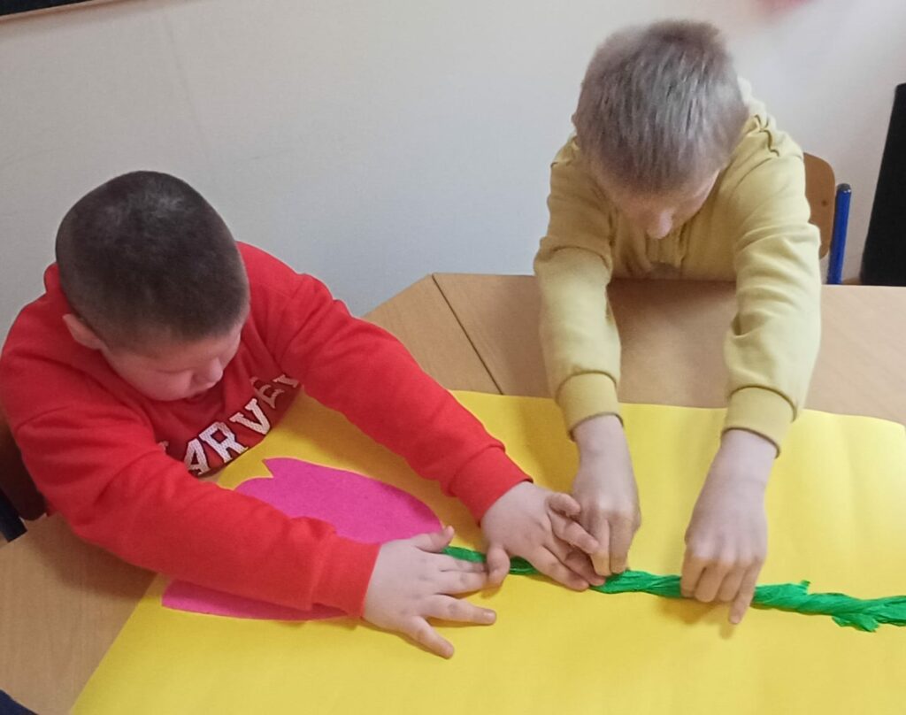 Dwóch chłopców dotyka naklejonego papierowego kwiatka.