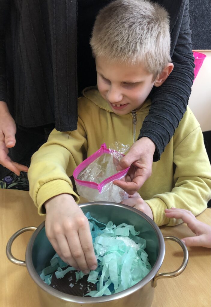 Chłopiec nasypuje sztuczny śnieg do metalowego garnka wypełnionego symbolami pogody.