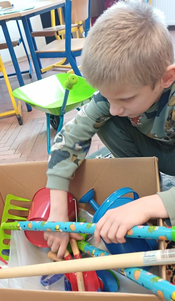 Chłopiec wyjmuje z pudełka narzędzia ogrodnicze.