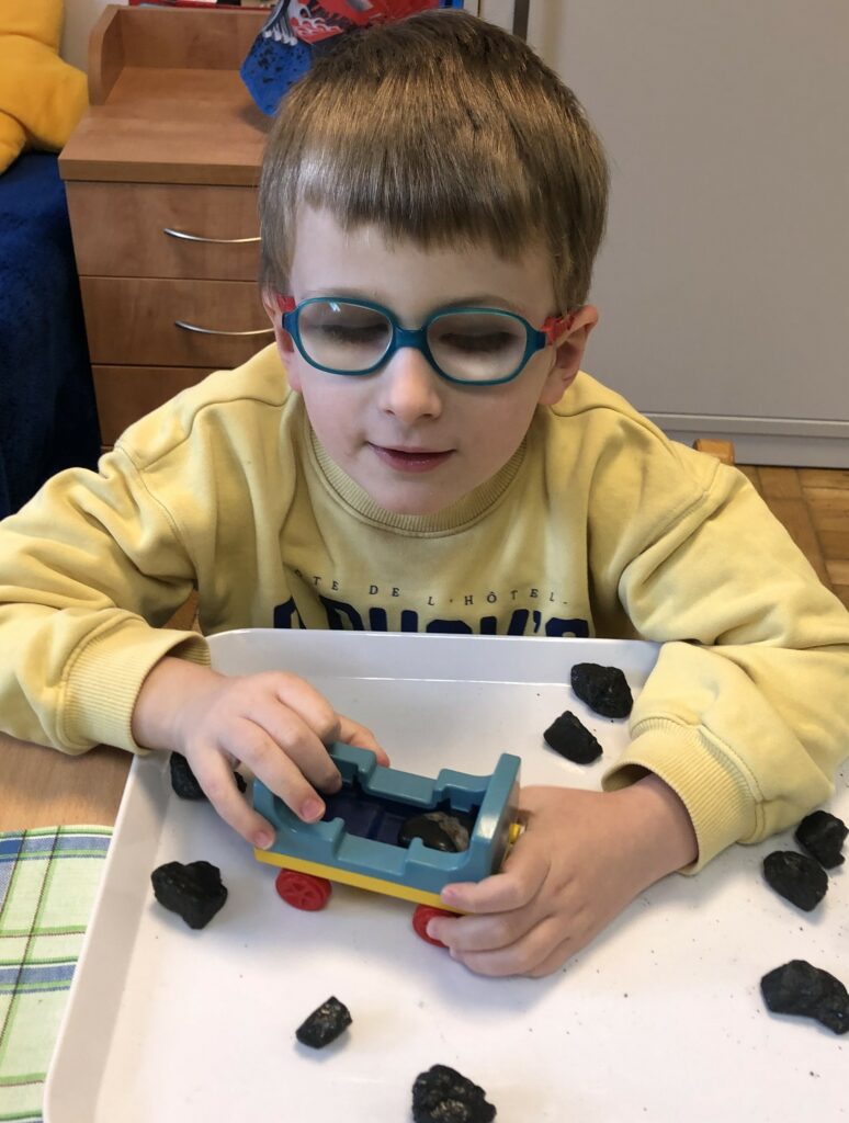 Chłopiec wkłada bryłki węgla do plastikowego wagonika.