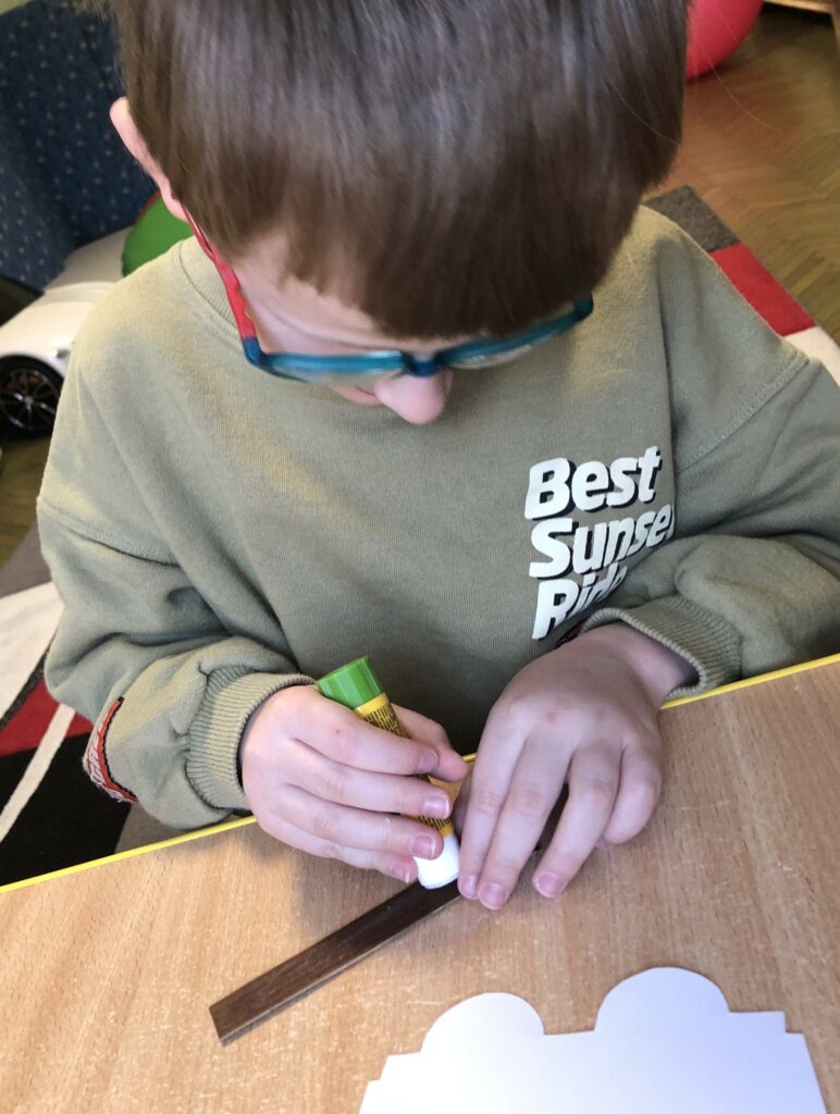 Chłopiec smaruje klejem papierowy element wagonika.