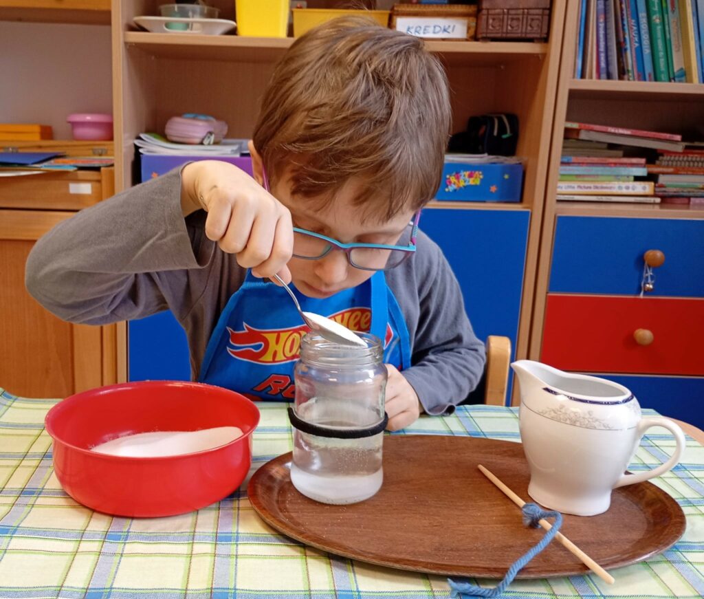 Chłopiec wsypuje sól do słoika z wodą.