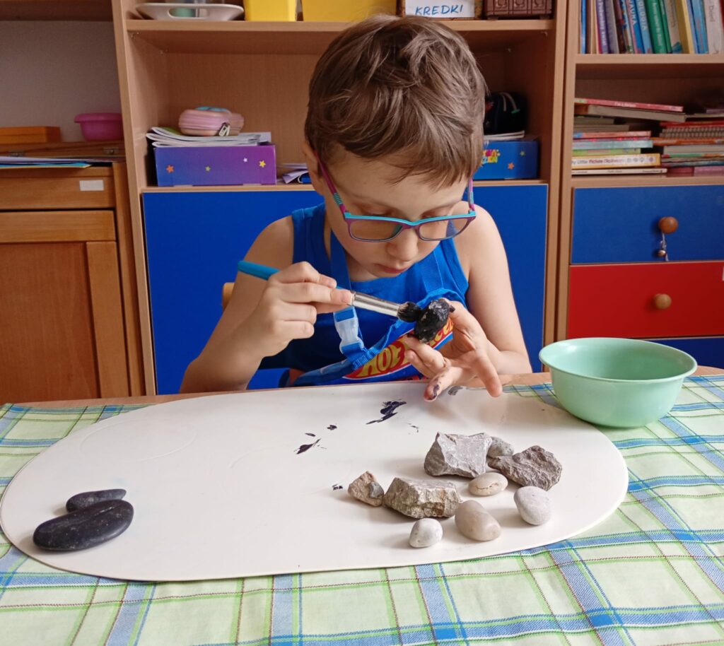 Chłopiec maluje kamienie na czarno.