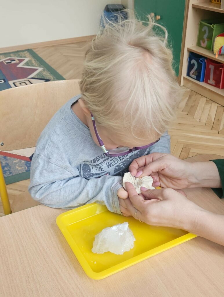 Chłopiec z pomocą nauczyciela zagląda do lnianego woreczka 