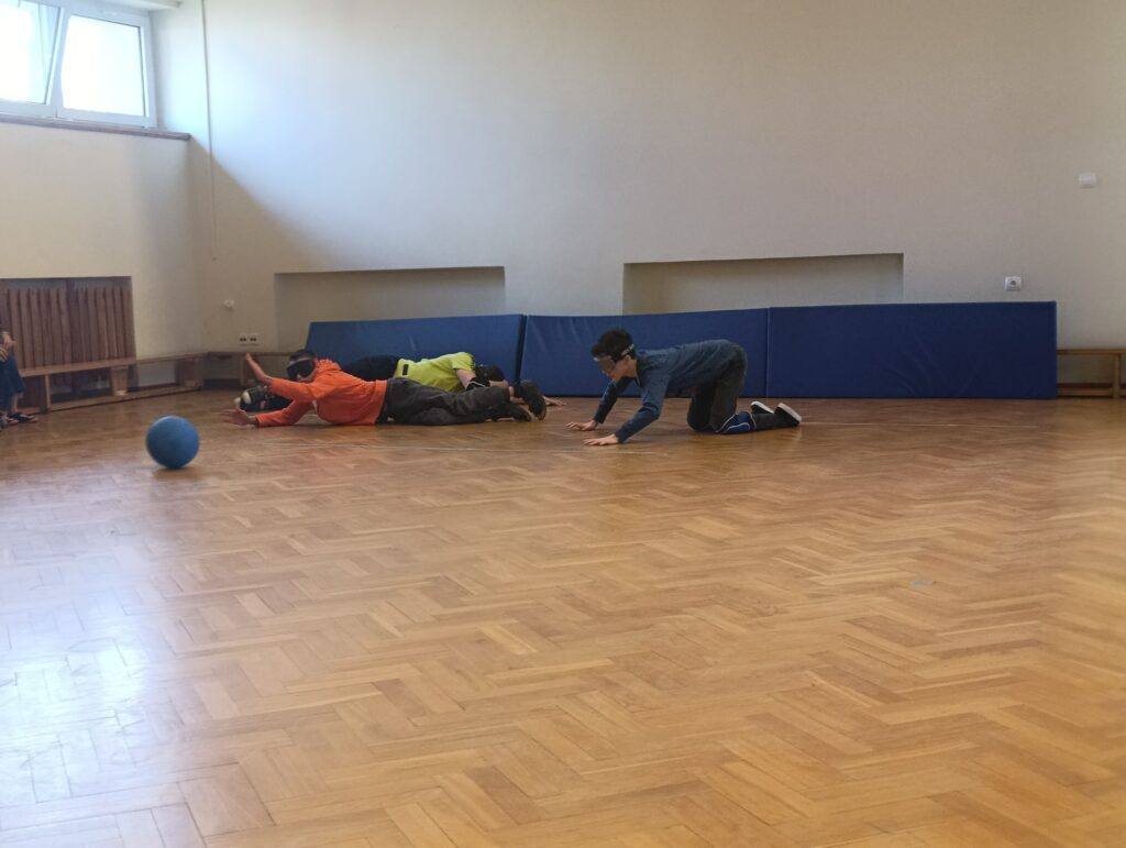 Podczas emocjonującego szkolnego turnieju w Laskach uczniowie w goglach startowych z wielkim zaangażowaniem rywalizowali na parkiecie, broniąc dostępu do bramki przed toczącą się dźwiękową piłką do goalballa.