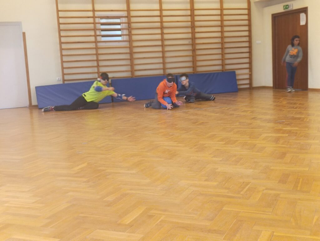 Zgrany zespół w goglach startowych czujnie osłania linię bramkową, zatrzymując piłkę dźwiękową podczas zaciętej rywalizacji w szkolnym turnieju goalballa.