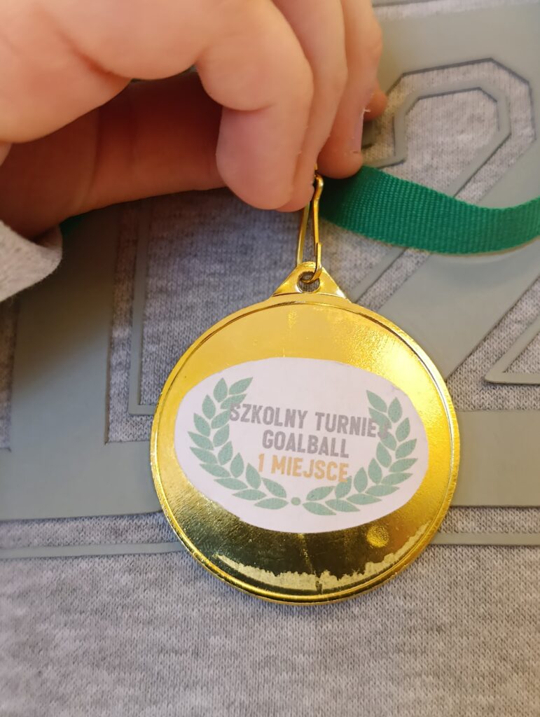 Złoty medal z napisem „Szkolny Turniej Goalball – 1 Miejsce” stanowi namacalny dowód sportowego sukcesu i wielkich emocji, jakie towarzyszyły uczniom podczas finałowych rozgrywek w Laskach.