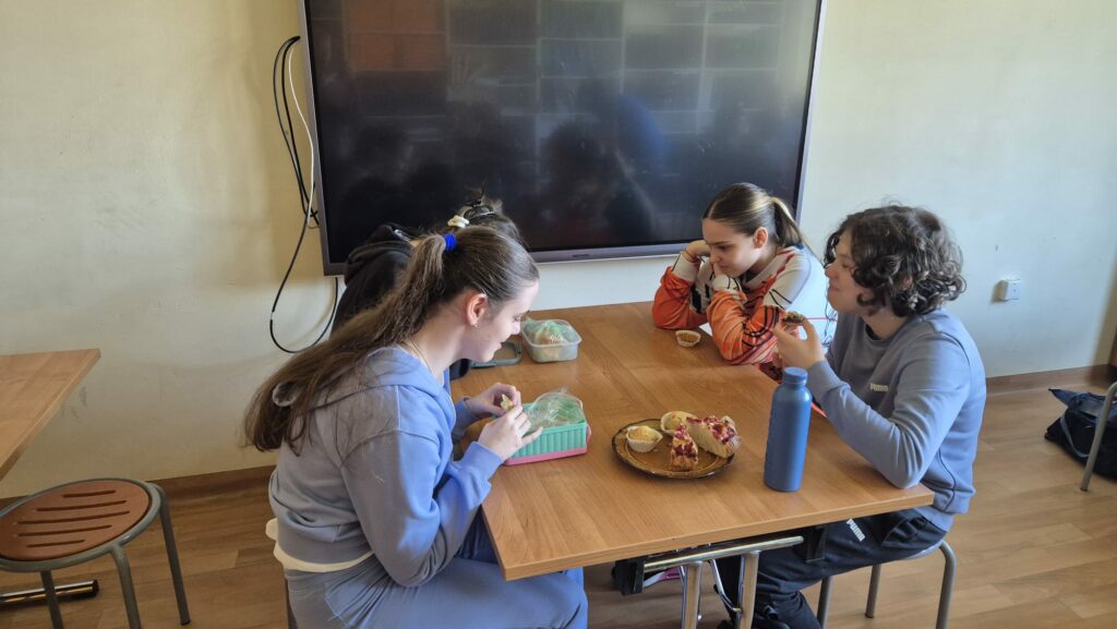 Uczniowie siedzą przy stole i jedzą wspólny posiłek