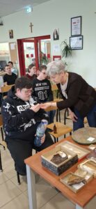 Zainteresowany uczeń z bliska analizuje autentyczny ząb drapieżnika podany przez prowadzącą, odkrywając fascynujący świat dawnych rekinów dzięki licznym eksponatom przygotowanym na wiosenne spotkanie przyrodnicze.