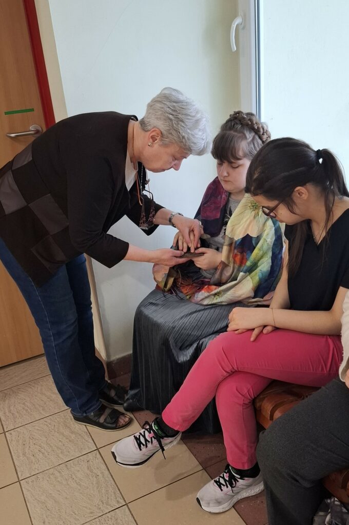 Nauczycielka pomaga uczennicom osobiście doświadczyć tekstury przyrodniczych eksponatów, umożliwiając im bezpośredni kontakt z autentycznymi fragmentami morskiego świata podczas wiosennego spotkania.