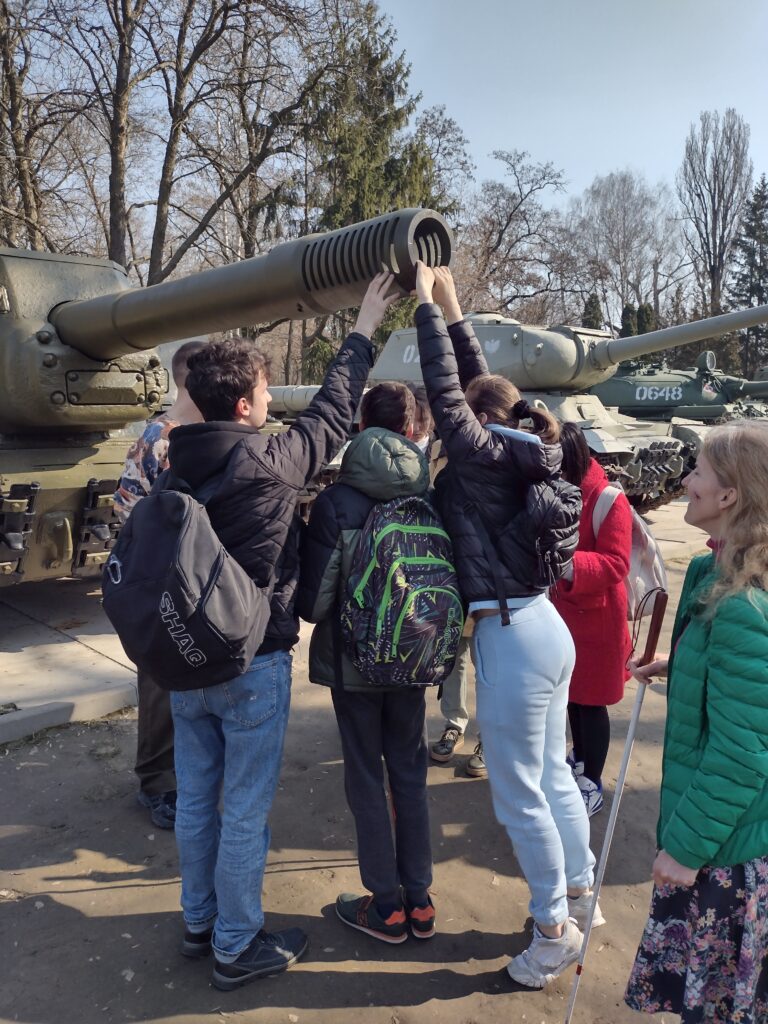 Grupa uczniów wspólnie bada konstrukcję lufy i hamulca wylotowego zabytkowego czołgu. Bezpośredni kontakt z ciężkim sprzętem wojskowym pozwala na lepsze zrozumienie techniki i historii militarnej.