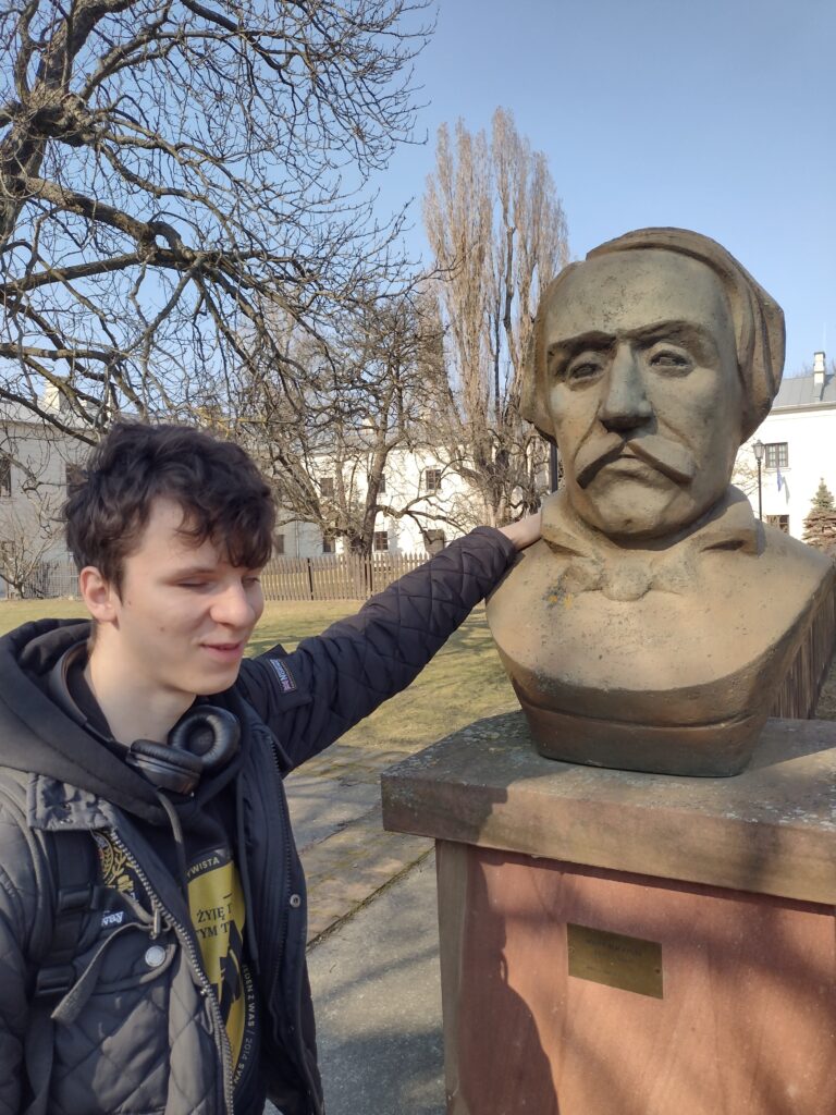 Uczeń szkoły ponadpodstawowej podczas zwiedzania terenu Cytadeli Warszawskiej zapoznaje się z pomnikiem-popiersiem, co stanowi element lekcji historii w plenerze, uzupełniającej wizytę w Muzeum Historii Polski.