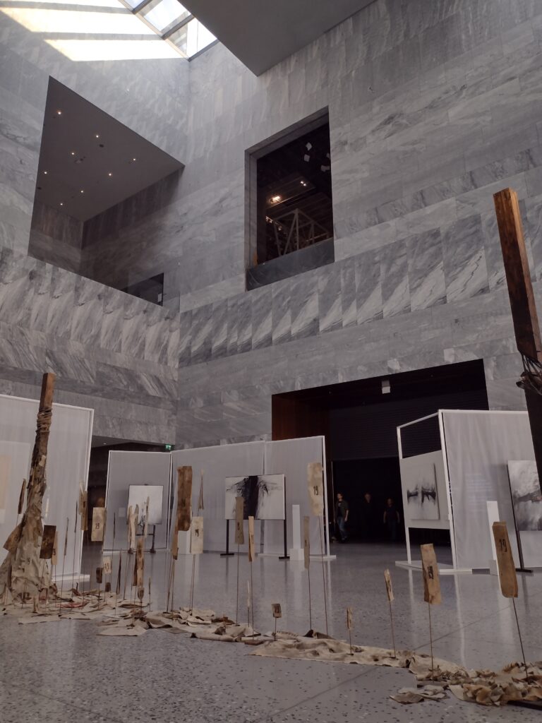 
Treść wiadomości Gemini
Wystawa czasowa „Gero Hellmuth. Przeciw zapomnieniu” została zaaranżowana w przestronnym i surowym wnętrzu Muzeum Historii Polski, gdzie gra świateł oraz pionowe elementy instalacji podkreślają monumentalny i refleksyjny charakter prezentowanych dzieł.