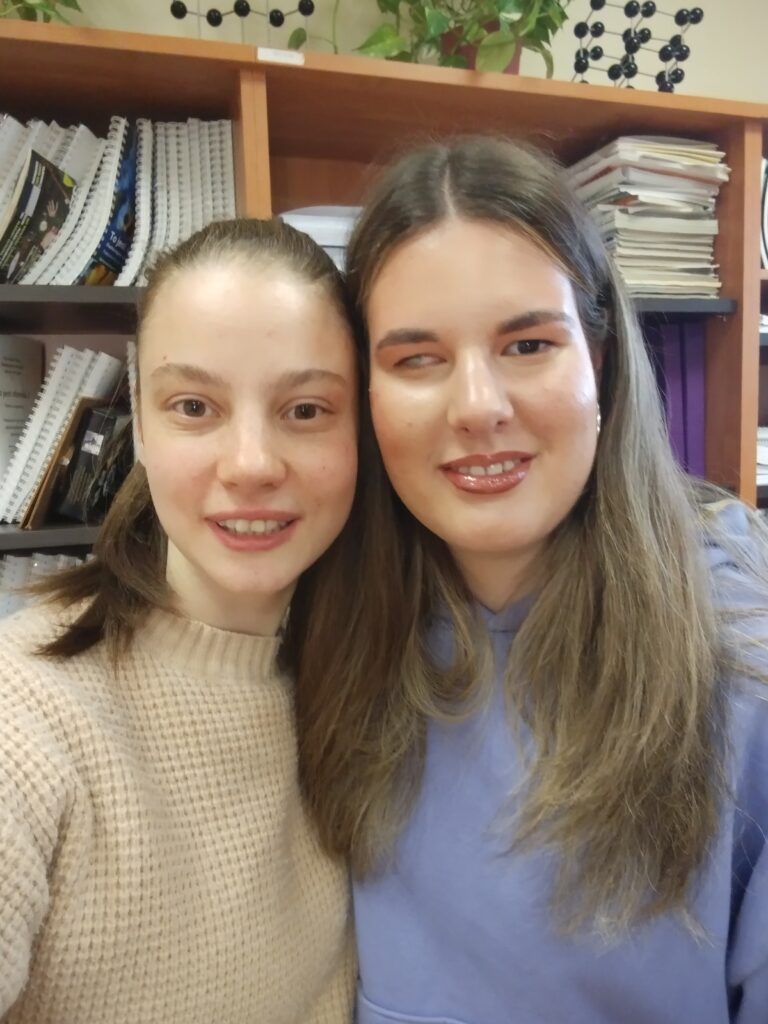 Dwie uśmiechnięte uczennice pozują do bliskiego portretu, prezentując efekty warsztatów: starannie podkreślone brwi, lśniące usta oraz delikatny makijaż oczu, który dodaje ich twarzom blasku i pewności siebie.