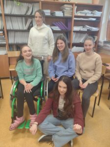 Na zdjęciu widać uśmiechniętą grupę pięciu uczennic z „Jabłonek” o promiennych, delikatnie umalowanych twarzach, które wspólnie pozują w radosnej atmosferze na tle regałów z książkami po zakończonych warsztatach makijażu.