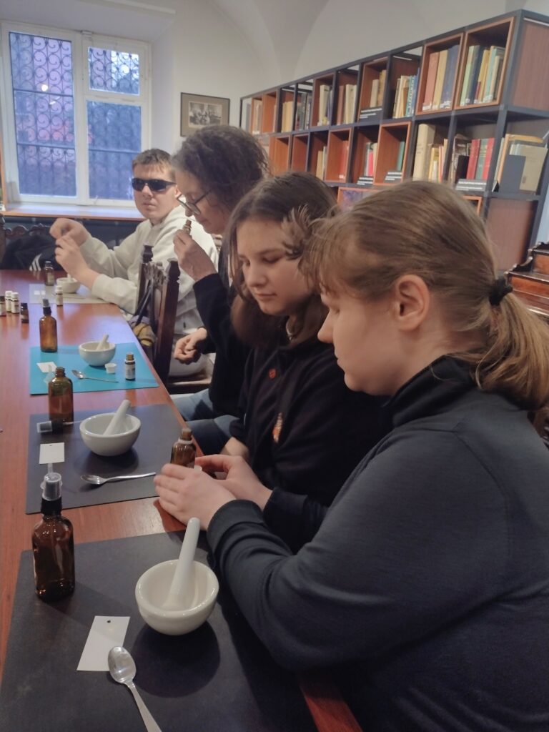 Uczniowie w pełnym skupieniu testują aromatyczne olejki, ostrożnie dobierając proporcje składników przy swoich stanowiskach, aby stworzyć wymarzone, harmonijne wody zapachowe.