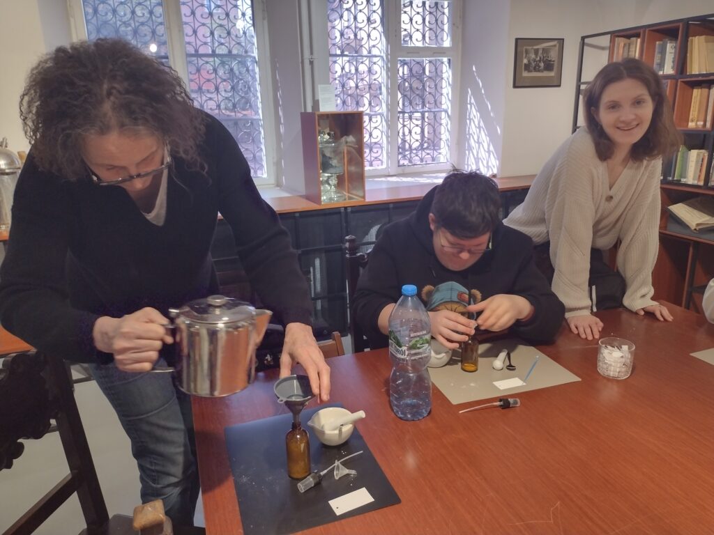 Podczas warsztatów w Muzeum Farmacji uczestnicy w skupieniu przelewają i mieszają esencje przy użyciu profesjonalnych naczyń, tworząc pod okiem instruktorki własne, unikalne wody zapachowe.