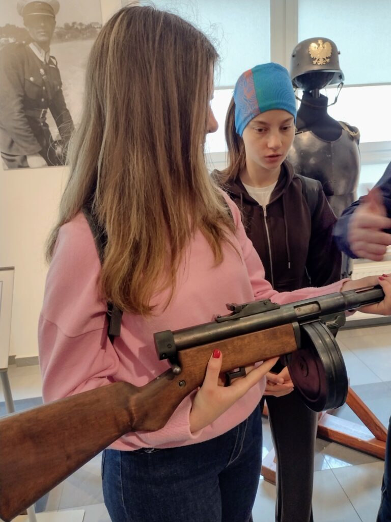 Uczestniczki wycieczki z uwagą oglądają zabytkową broń palną w Wydziale Edukacji Historycznej GKGP, poznając z bliska elementy dawnego wyposażenia formacji policyjnych.