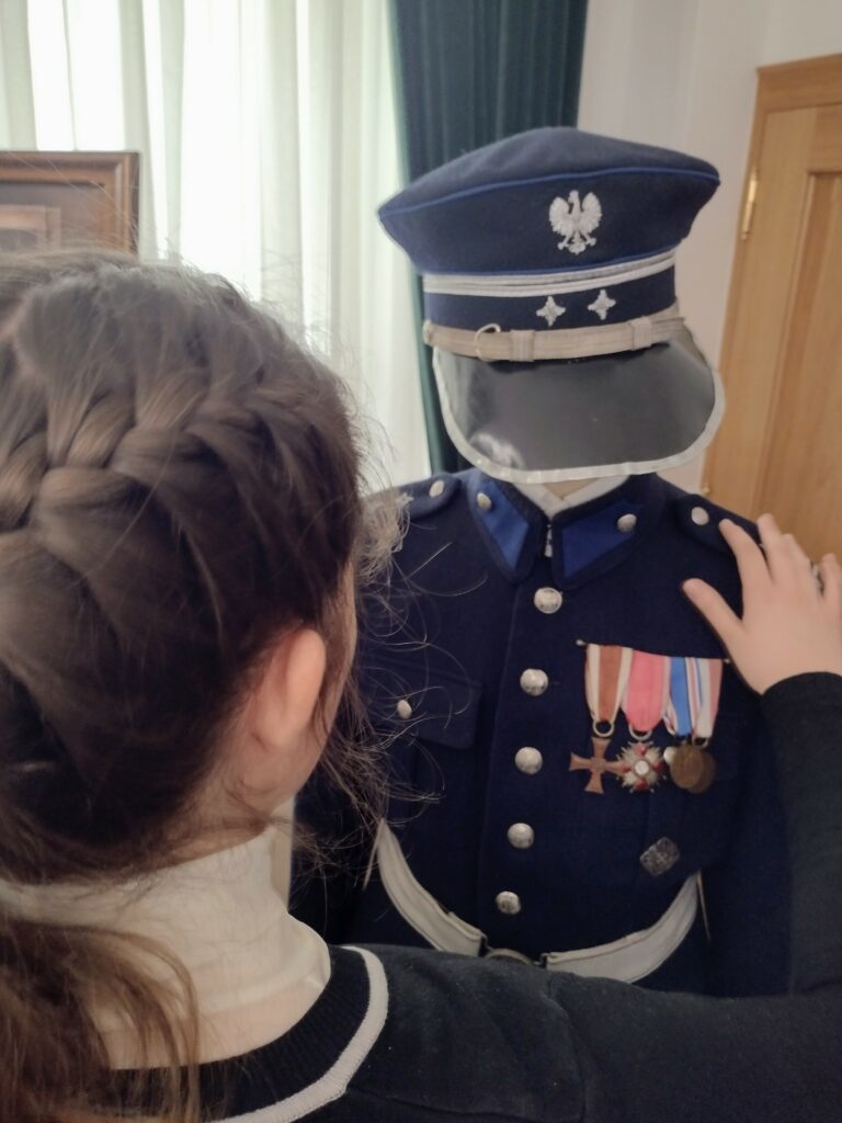 Uczestniczka wycieczki, odwiedzając Wydział Edukacji Historycznej GKGP, ma okazję z bliska przyjrzeć się historycznemu umundurowaniu Policji Państwowej, poznając detale dawnych dystynkcji i odznaczeń.