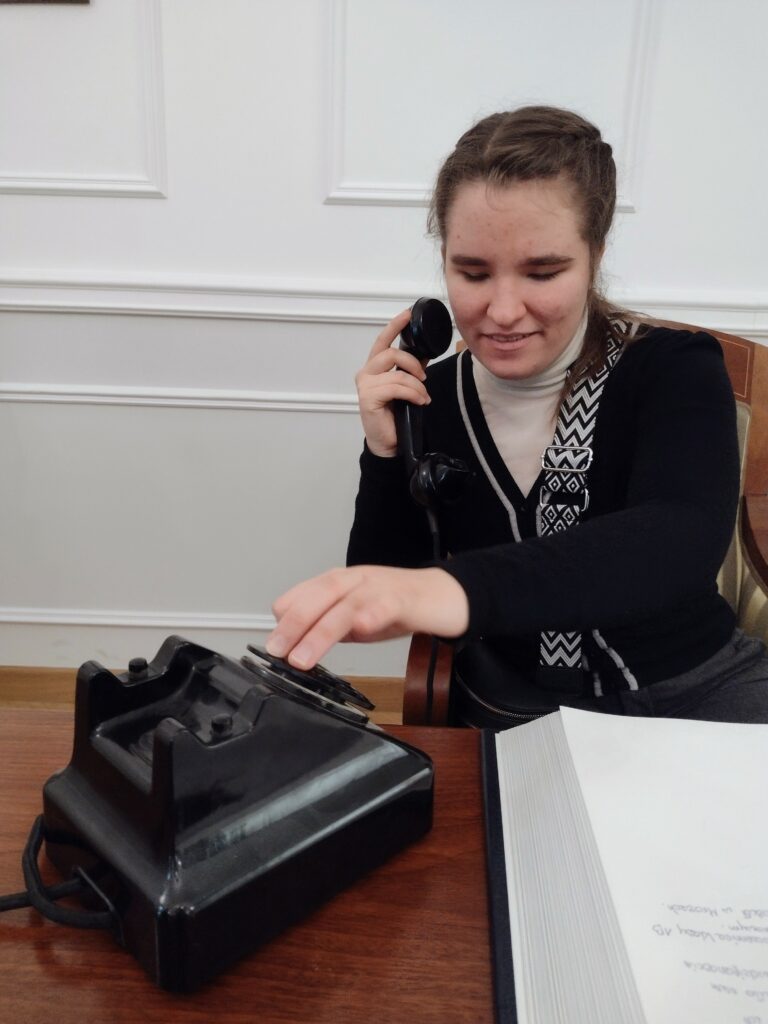 W Wydziale Edukacji Historycznej GKGP uczestniczka wycieczki z zainteresowaniem odkrywa dawną codzienność pracy policjantów, próbując swoich sił w obsłudze zabytkowego telefonu z tarczą numerową.