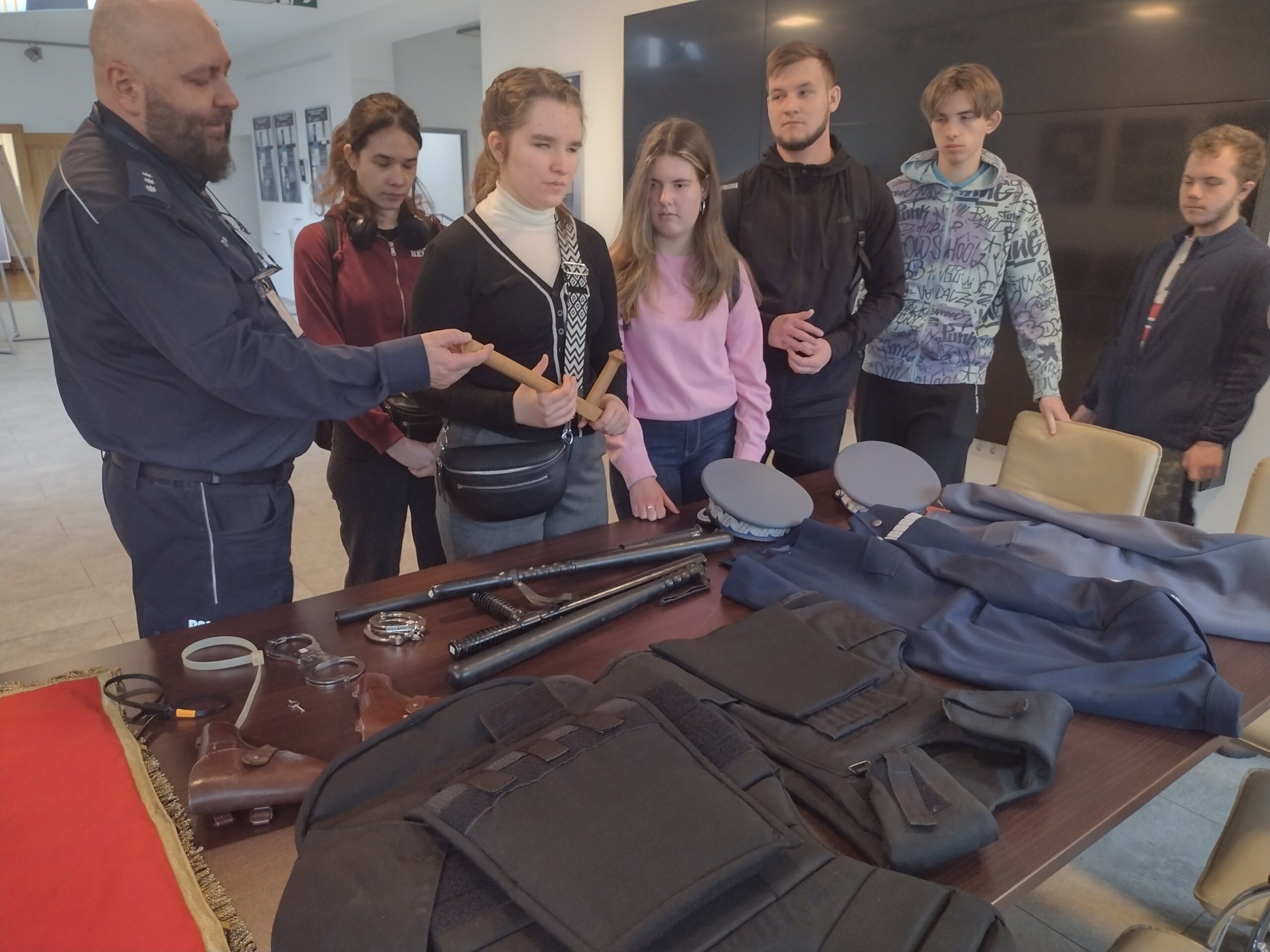 Podczas spotkania w Wydziale Edukacji Historycznej GKGP uczestnicy z zainteresowaniem oglądają dawne i współczesne wyposażenie policyjne, w tym kajdanki, pałki oraz kamizelki kuloodporne, słuchając przy tym opowieści o codziennej pracy funkcjonariuszy.